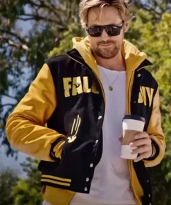 Ryan Gosling wearing The Fall Guy black and yellow varsity jacket with a yellow hoodie and sunglasses. Perfect yellow varsity jacket mens style.