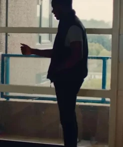 Side silhouette of Tazer in a black vest and dark trousers, standing near a window on a balcony or walkway.