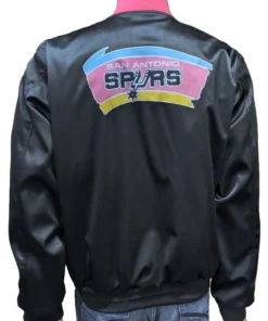 Back view of a black satin San Antonio Spurs pregame jacket featuring the vintage pink, orange, and teal logo and NBA Spurs warm up jacket style.