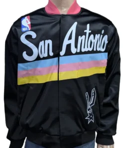 Front view of a San Antonio Spurs warm up jacket for men and women with teal, pink, and yellow stripes and San Antonio script across the chest.