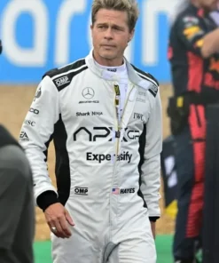 Brad Pitt wearing the Grand Prix Brad Pitt F1 Racing Jumpsuit in a Formula One pit lane, showcasing the sleek white and black racing suit design.