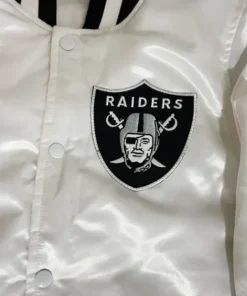 Close-up shot of the front chest pocket on a white Raiders jacket featuring the embroidered Raiders shield logo patch.