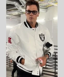 Tom Brady wearing the Las Vegas Raiders white jacket (a white bomber jacket style) while walking, with his hands in the pockets.