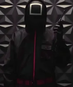 Image of a person wearing the Squid Game black guard suit holding a walkie-talkie, featuring the distinctive black square mask and the hooded black uniform with pink accents. This is a great representation of the black square guard.