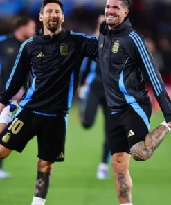 Lionel Messi and Rodrigo De Paul stretching, both wearing the Messi Argentina football hoodie, black with blue accents, ideal for supporters of Argentina's last home game or a Messi Argentina match day hoodie.