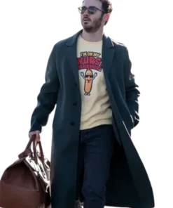 Kevin Jonas in a dark forest green peacoat over a striped shirt, looking off-camera while holding a small black object, possibly a phone.