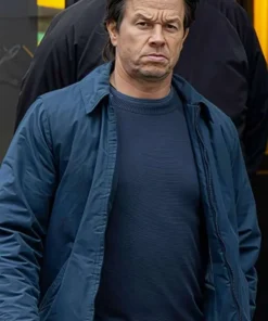Mark Wahlberg sporting The Family Plan 2 blue jacket, walking with a serious expression