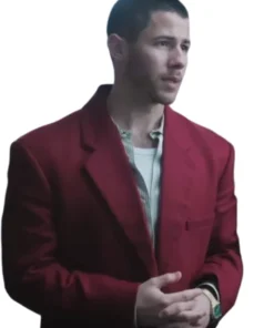 Close-up of Nick Jonas wearing a bold red blazer over a pale, striped collared shirt that's open at the neck. He is looking off to the side with his hands clasped in front of him.