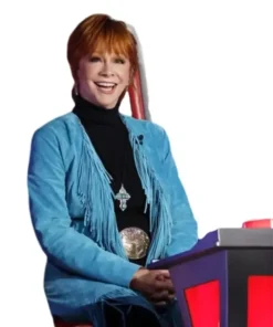 Reba McEntire blue suede fringe coat on The Voice S28, smiling and wearing a large western belt buckle.