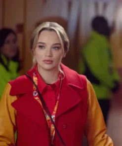 Close-up of actress Alana Higman with her hair half-up, wearing a red coat with yellow or gold varsity-style sleeves and a red button-down shirt. She has a patterned yellow and red lanyard around her neck.