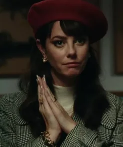 Close-up of Kaya Scodelario in a tartan trench coat and red beret, wearing a luxurious plaid coat with pearl earrings.