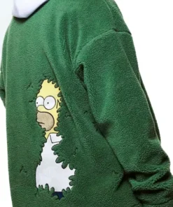 A close-up shot of a person wearing an oversized, dark green sherpa fleece jacket, zipped up halfway over a white hooded sweatshirt. The jacket has the embroidered white text 