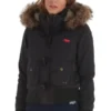 A young woman posing in a short, black Superdry Study Duffle Jacket. The jacket is a puffer style with a ribbed waistband and cuffs, large front flap pockets with toggle closures, and a hood trimmed with thick brown Vegan fur. The red embroidered Superdry logo is visible on the chest.