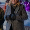 Smiling woman wearing a grey herringbone double-breasted winter coat with black gloves and a high-neck top in a snowy holiday setting.
