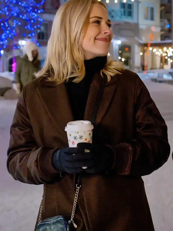 A medium shot of Alexandra Breckenridge standing outside in the snow, wearing a brown coat and black gloves, holding a holiday-themed coffee cup.
