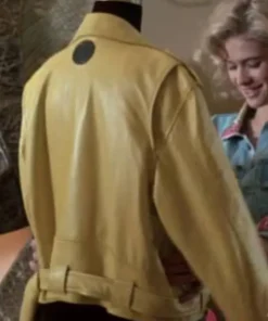 Back view of the yellow leather jacket displaying a distinctive black circular patch on the upper back, with actress Kristy Swanson visible in the background.