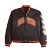 Front of a dark brown Cleveland Browns satin varsity bomber jacket with "BROWNS" across the chest and vertical numbers "50," "55," "64" on the left sleeve.