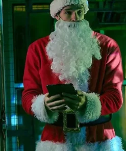 Connor Swindells wearing a red Santa coat with white fur trim and beard, holding a tablet in a festive indoor setting.