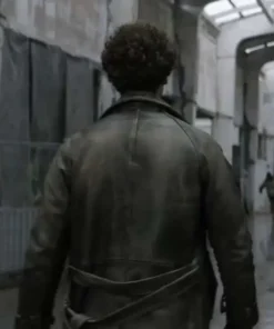 Back view of Emile's distressed leather coat, showing the waist belt and yoke, as he walks away down an abandoned, grim hallway.