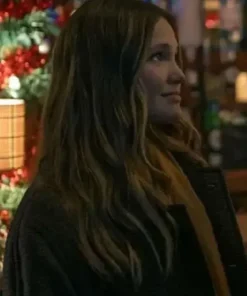 Olivia Holt Jingle Bell Heist brown coat. Side profile of Sophia (Olivia Holt) with wavy hair, wearing the Brown Long Coat near a festive, lit holiday display.