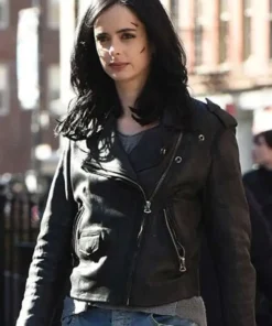Krysten Ritter as Jessica Jones in a medium shot, wearing her asymmetrical black leather jacket and looking serious, with marks visible on her face.