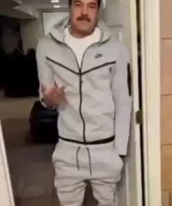 A full-body shot of a man with a mustache who resembles Nicolás Maduro, wearing a light grey Tech Fleece tracksuit. He is standing in a doorway indoors, gesturing with one hand.