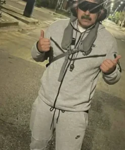 A man with a mustache, looking like Nicolás Maduro, standing outdoors at night. He is wearing a grey Tech Fleece tracksuit, blacked-out goggles, and large earmuff-style headphones, giving two thumbs up.