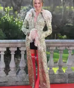 Margot Robbie wearing a John Galliano long trim coat in vintage floral brocade with pink feathered trim on a red carpet.